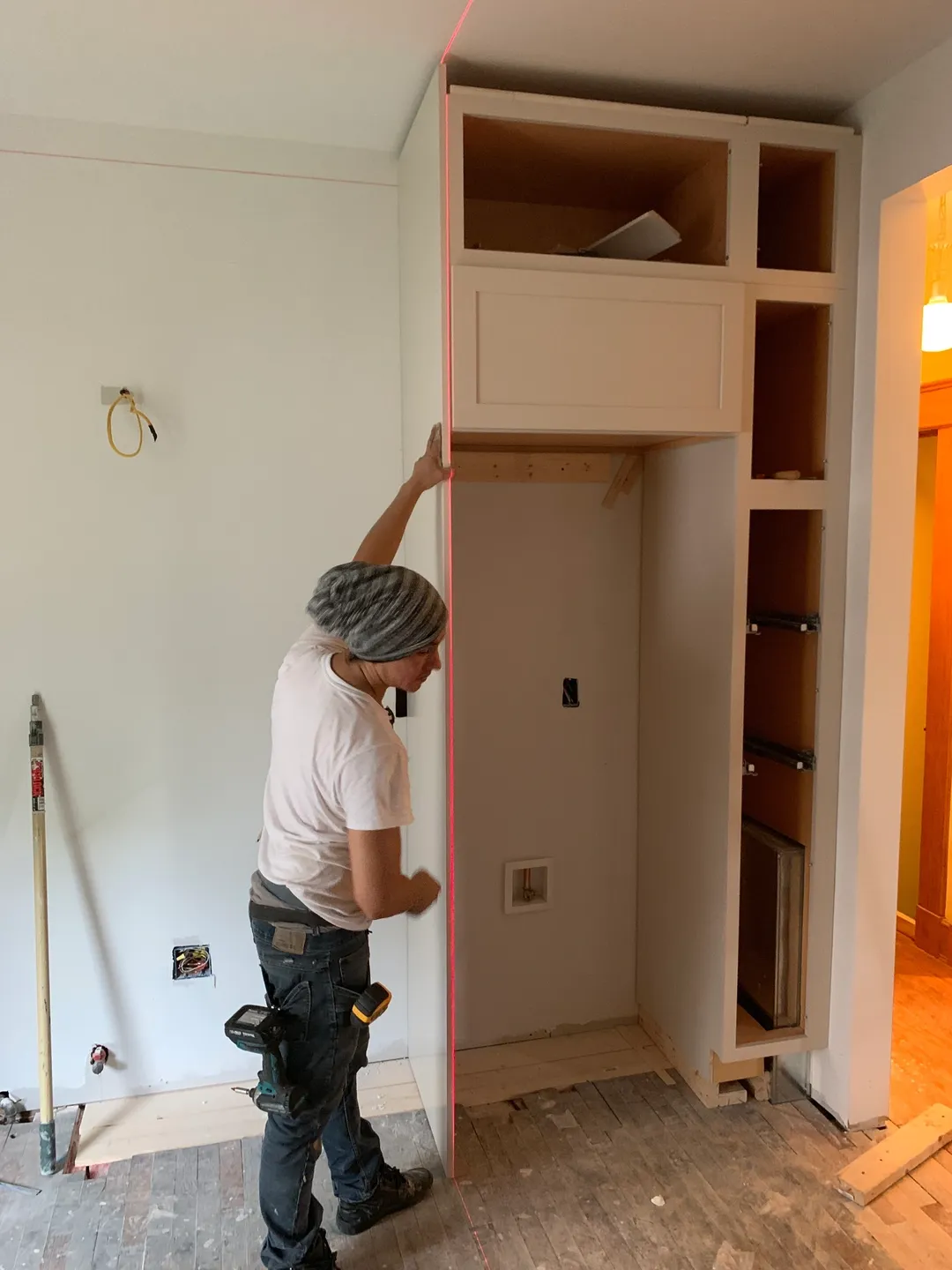 A man is working on the wall of his kitchen.