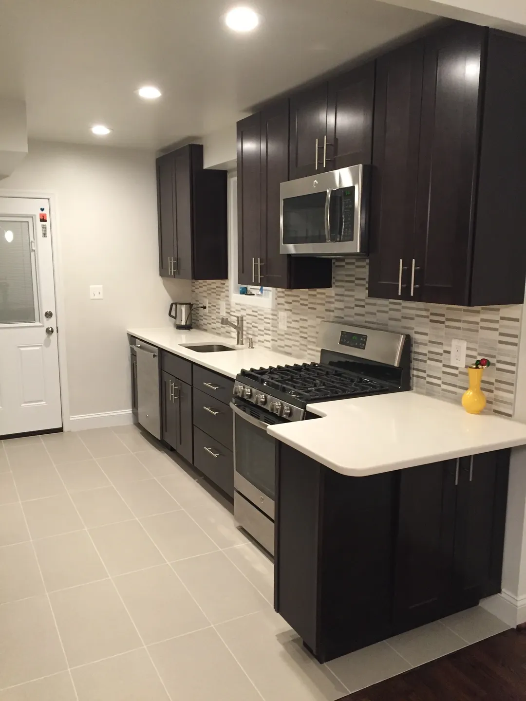 A kitchen with dark cabinets and white counters.