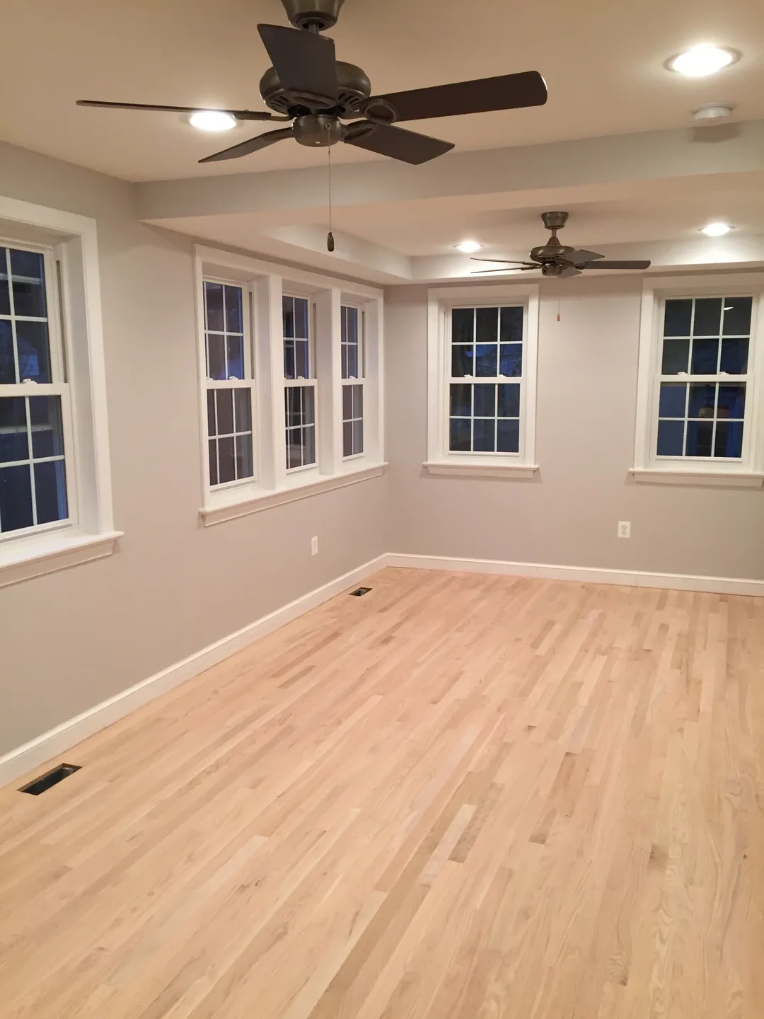 A room with two windows and a ceiling fan.