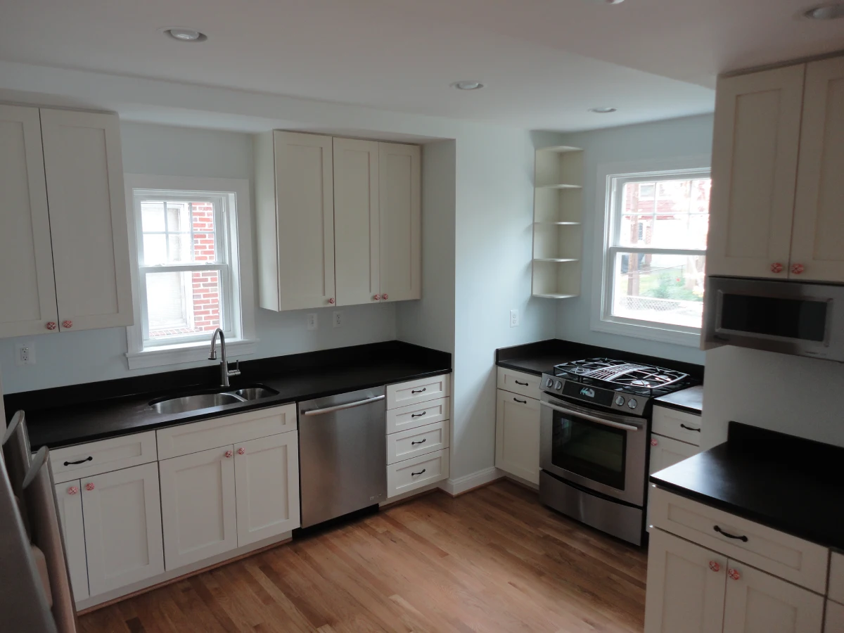 A kitchen with white cabinets and black counter tops.